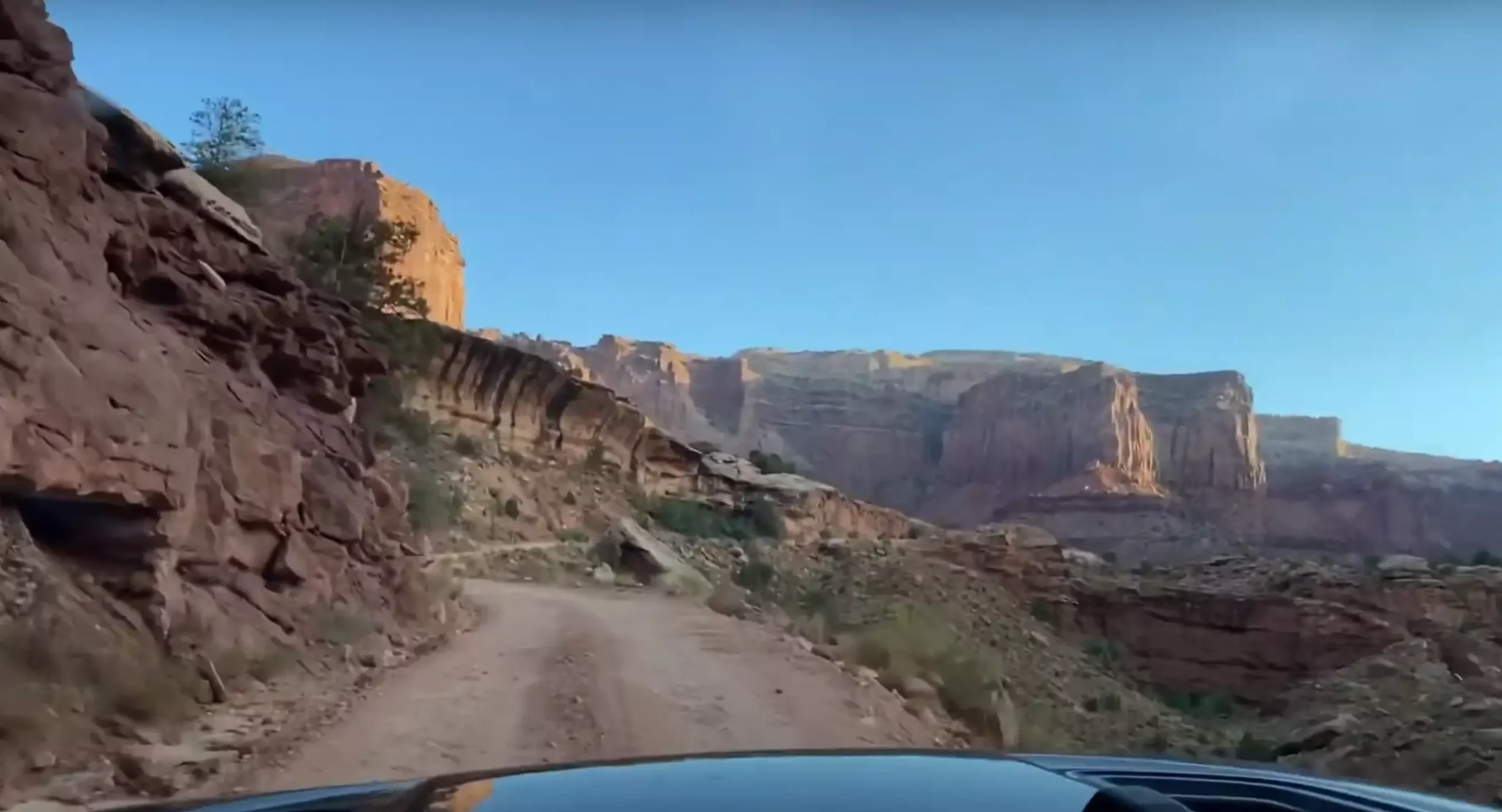 From the cockpit of a Jeep Wrangler on Shafer Trail, you're enveloped by towering crimson canyons under a brilliant azure sky. The rugged trail beckons, a dirt ribbon of adventure, as you grip the wheel with anticipation. This is raw, untamed beauty at your fingertips, each twist revealing a mesmerizing landscape etched in the heart of the American Southwest.