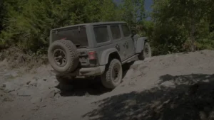 A rugged, off-road Jeep Wrangler with its signature boxy design and removable doors and roof, navigating through rocky terrain